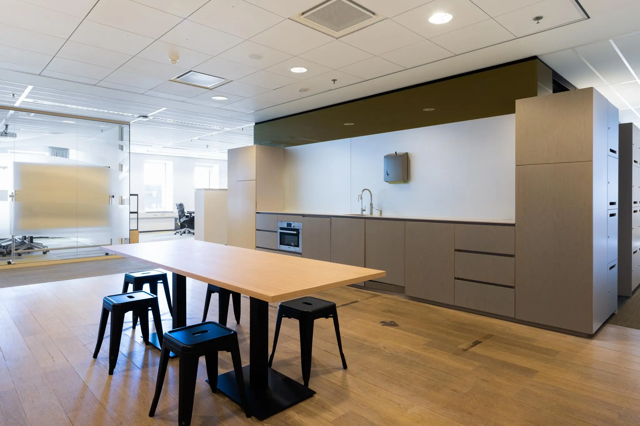 Moderne kantoorpantry aan de Prinses Beatrixlaan met een houten tafel, zwarte krukken en ingebouwde keukenapparatuur.